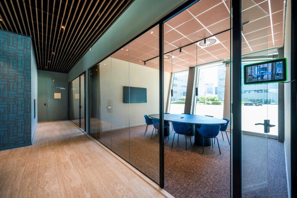 Moderne vergaderruimte aan de David Ricardostraat met glazen wanden, blauwe stoelen en uitzicht op kantoorgebouwen.